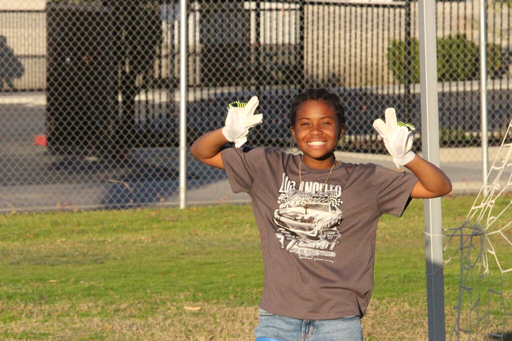 Smiling child wearing gloves during a community activity organized by the Power of Water Foundation, reflecting empowerment, purpose, and active youth engagement.